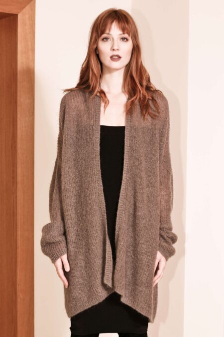Woman modeling a brown NOELLE chunky ribbed cardigan with an open front and extra-long sleeves, styled over a fitted dress, standing against a neutral background.