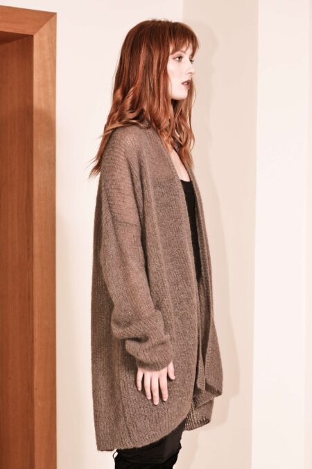 Woman modeling a black NOELLE chunky ribbed cardigan with an open front and extra-long sleeves in a 3/4 side view, styled over a fitted dress, standing against a neutral background.
